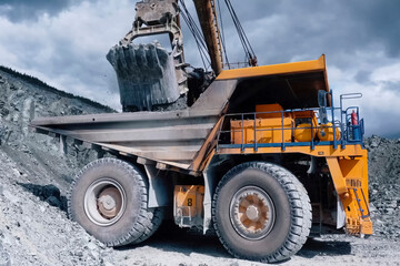 Yellow mining dump truck with crushed stone in body, industrial