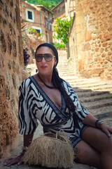 A woman in a zebra print dress sits on a stone wall with a straw bag on her lap