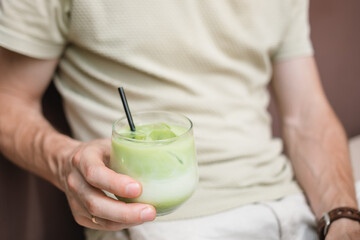 Close-up of a man sitting outdoors in summer drinking an iced matcha latte.