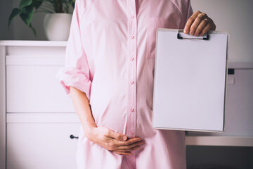 Pregnant woman with empty white paper as medical card, agreement blank. Template for text.