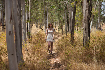 Young woman, beautiful, blonde, wearing a floral dress, relaxed and calm, walking among the trees, in connection with nature and ecology, in an outdoor park. Concept of beauty, youth, millennial.