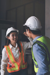 Construction manager and engineer dressed in orange work vests and hard helmets explore construction documentation on the building site near the steel frames