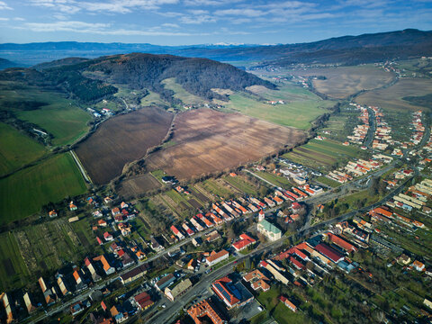 Aerial view of a patchwork of fields and rooftops nestled against the backdrop of rolling hills, painting a serene landscape, Detva, Bansk&Atilde;&iexcl; Bystrica Region, Slovakia.