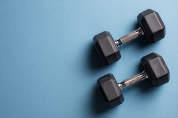 Black dumbbells on a blue background, top view. Space for text or copy space