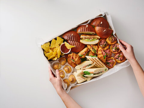 A vibrant assortment of snacks including sliders, taquitos, and nachos is shared among friends at a casual lunch gathering. The table is set with an inviting atmosphere
