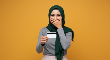 Happy Young Woman in Hijab Holding Credit Card and Covering Mouth With Hand