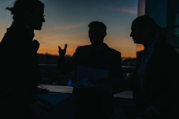 Business people are seen in silhouette, engaging in a thoughtful conversation against a vibrant...