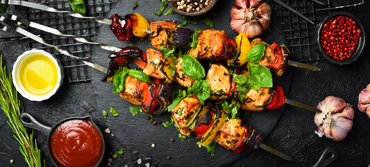 Shish kebab from chicken breast, and grilled vegetables on metal skewers. Top view. On a black background.