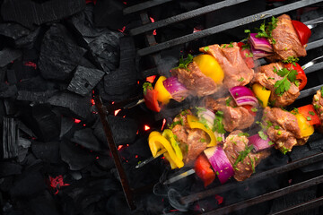 Raw Pork Skewers with Vegetables on a grill grate, over hot charcoal. Top view. On a black textured...