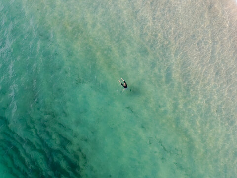 Aerial view of a lone figure floating serenely in the turquoise waters, a stark contrast to the sandy seabed below, Fowey, Cornwall, United Kingdom.