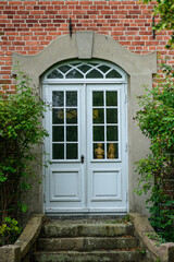 window in a stone wallfull-frame shot of an old, weathered wooden door painted in a soft gray color, set within a rustic brick archway. The door is adorned with multiple glass panes 