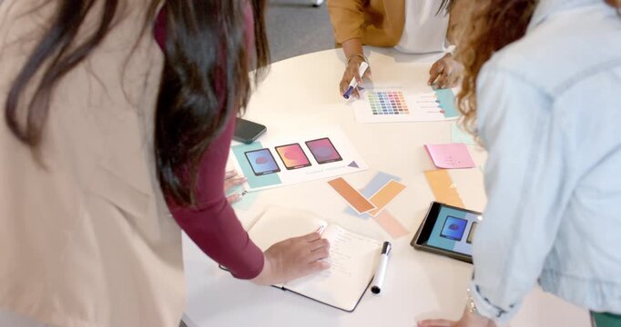 Post briefing Diverse female colleagues arranging swatches and noting codes at table for review