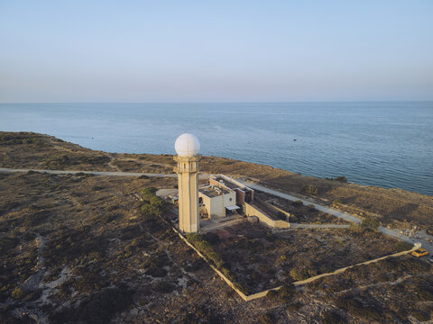 Aerial view of a stark white radar dome perched atop a weather station, contrasting against the blue sea and arid landscape, Leucate, Occitanie, France.