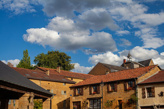 Scenic view of rustic stone houses with red-tiled roofs in Torgny, Belgium. Bright blue sky with fluffy clouds adds charm to this picturesque village in the Gaume region.