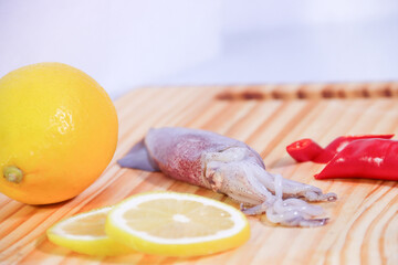 Squid with Whole and Sliced Lemons on Wooden Cutting Board with Red Chili