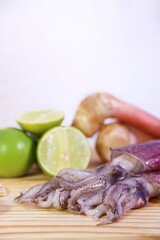 Three Squids on Wooden Cutting Board with Blurred Lime and Galangal