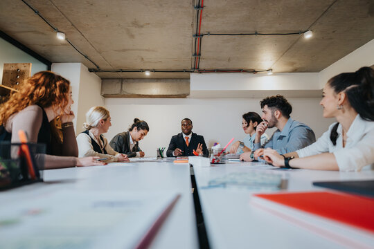 A team of business people sits around a conference table engaging in an interactive discussion, emphasizing collaboration and teamwork within a modern work environment.