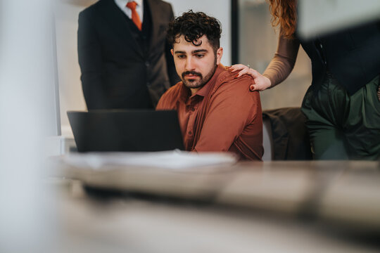 A group of coworkers engaged in a focused discussion, working together in a modern office environment. One appears absorbed in his task as others provide support and encouragement.