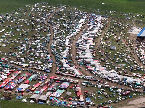 Aerial view of a vibrant festival sprawling across a vast green field, dotted with colorful tents and bustling crowds, Sichuan, China.