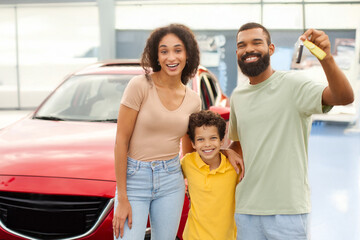 Joyful black family showing new car key, standing near auto outdoor, parents and son celebrating...