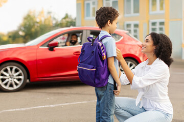 Young Latin mother talking to her son in front of car on parking before send child boy to school,...