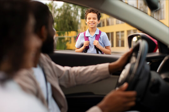 Mother and father dropping off son coming to school in the morning, schoolboy smiling to parents, view from inside auto