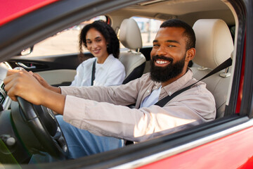 Happy Black couple smiling from car window, excited man and woman sitting in auto after test drive...
