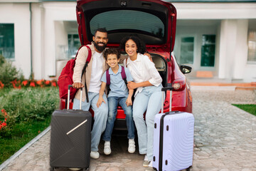 Family prepare and packing luggage ready to travel, parents and their son sitting in car trunk and smiling at camera, full length shot © Home-stock