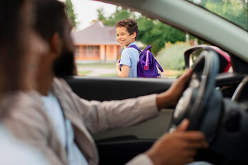 Parents brought their son to school, schoolboy turning back and smiling to parents, view from inside auto