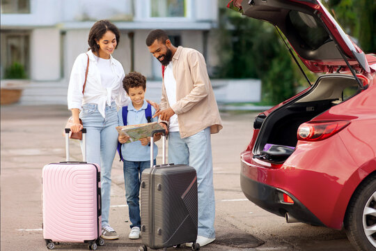 Family of three ready for the travel for vacation, standing with suitcases and paper map near car, father and son discussing and planning route