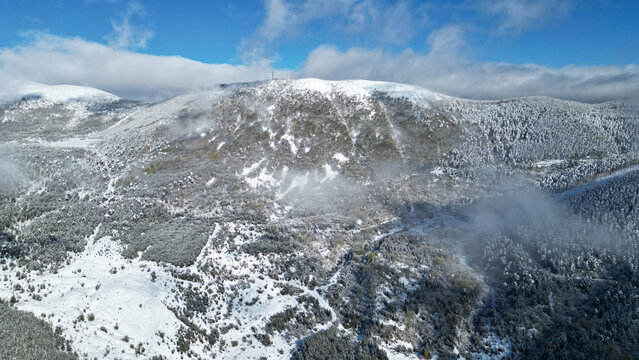 Aerial view of a snow-dusted mountain peak piercing through a veil of mist under a crisp blue sky, Posof, Ardahan, T&Atilde;&frac14;rkiye.