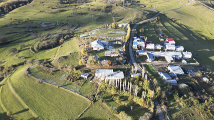Aerial view of a village nestled amid rolling green hills, touched by early winter's frost, Posof, Ardahan, TÃ¼rkiye.