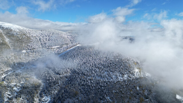 Aerial view of snow-dusted mountain peaks piercing through a veil of clouds under a crisp blue sky, Posof, Ardahan, T&Atilde;&frac14;rkiye.