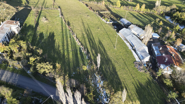 Aerial view of long shadows stretch across the verdant fields, contrasting with the snow-dusted ground and outlining the rooftops of scattered buildings, Posof, Ardahan, T&Atilde;&frac14;rkiye.