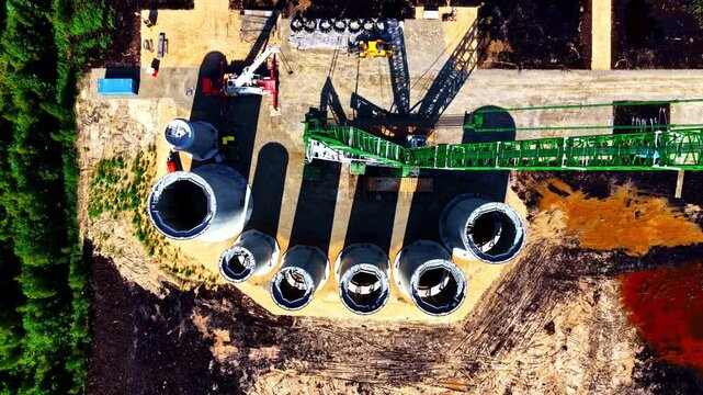 Wind park construction site, revealing multiple massive concrete turbine bases in various stages of assembly, heavy cranes and construction equipment - A dramatic straight-down aerial rise