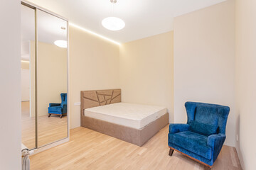 Modern bedroom with minimalist design featuring a blue armchair and a bed without linens