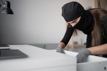 Burglar, robber or thief breaks home. Woman wearing black balaclava stealing things from house or...
