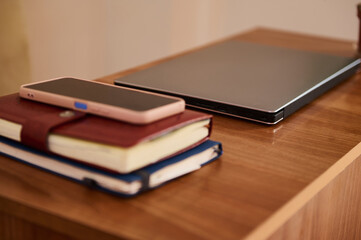 Modern Workspace with Closed Laptop, Smartphone, and Notebooks on Wooden Table