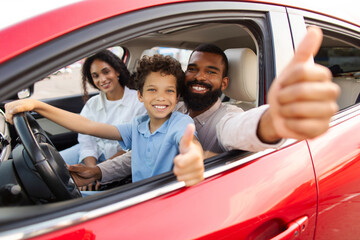 Latin family approving new car, father and preteen son gesturing thumbs up, boy sitting on dad lap on drivers seat. We like our auto