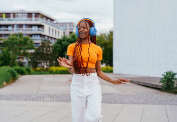 Fototapeta premium Joyful young woman with blue headphones dancing on city street