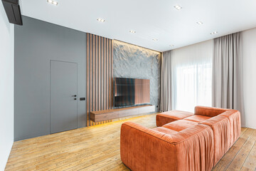 Modern living room with orange sofa and minimalist decor featuring a television on the wall