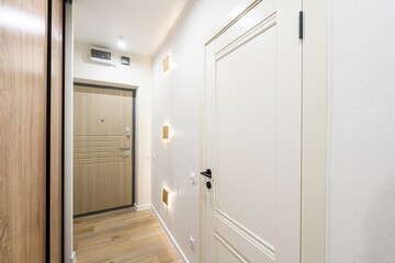 Bright hallway with light wood flooring, white walls and doors. Features a wooden entrance door, a...