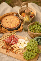 Picnic on nature with grapes, cheese and pie on blanket, enjoying summer outdoors, rustic countryside vibes and delicious food in a relaxed setting.