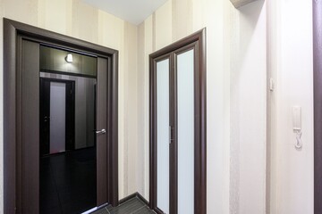 Photo shows a hallway with doors. One door is open, revealing a dark room. The hallway has striped...