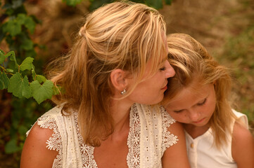 Mother kissing her little daughter sitting beside her, showing tender family bond, love, affection...