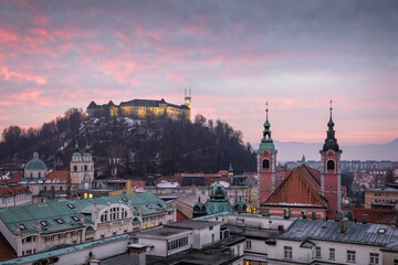 Ljubljana cityscape with castle and cathedral towers under colorful sunrise sky