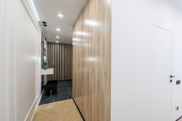 hallway with a mix of textures and colors. It shows a wooden wardrobe, white walls, a black marble...