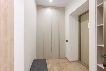 well-lit entryway features built-in storage, a bench, and beige stone flooring. Neutral tones create a clean, modern aesthetic