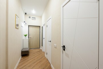 hallway with wooden flooring and beige walls. There are several white doors with dark handles and a...