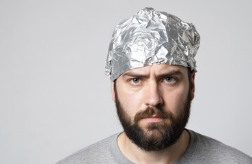 Fototapeta premium Suspicious bearded man wears tinfoil hat, believes in conspiracy theories. Distrustful, skeptical look. Concept of paranoia, eccentricity, unusual behavior, odd, strange secretive personality,